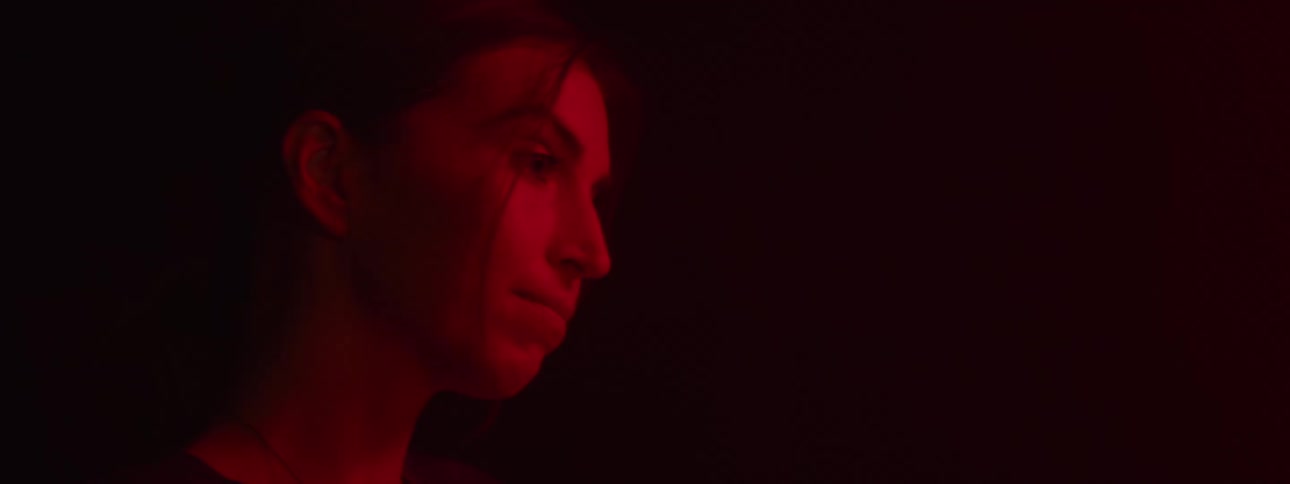 A young woman stands in a dark room illuminated by red fluorescent light with a smile on her face