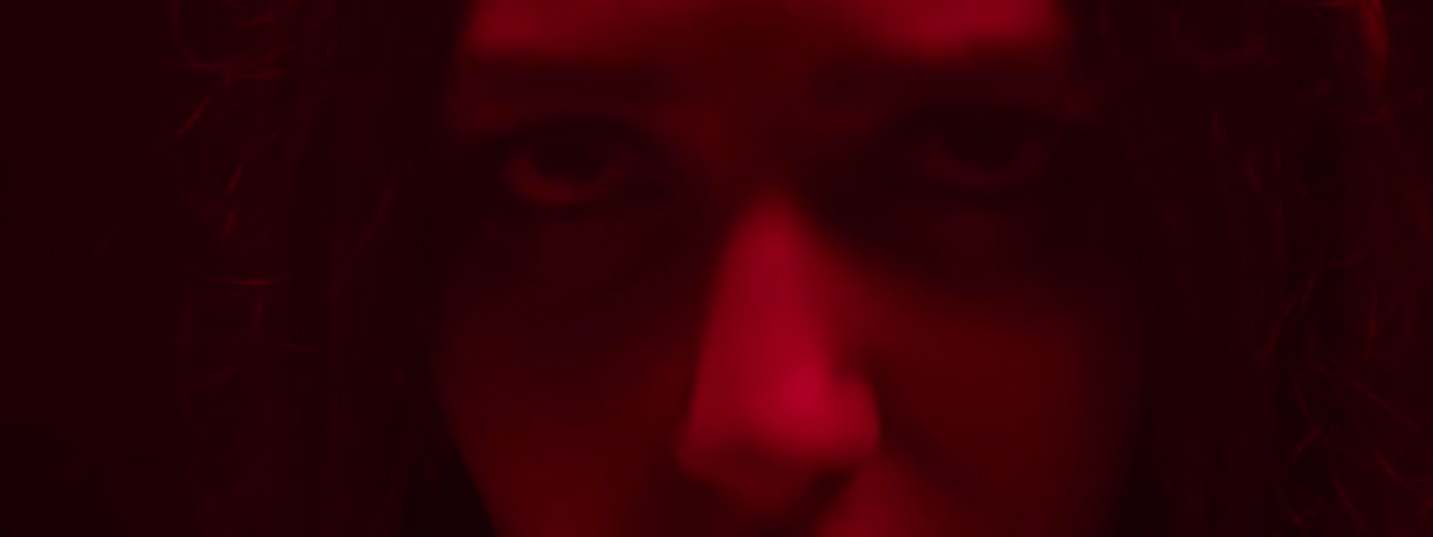A young woman folds her fist around some money while in a dark room illuminated by red light