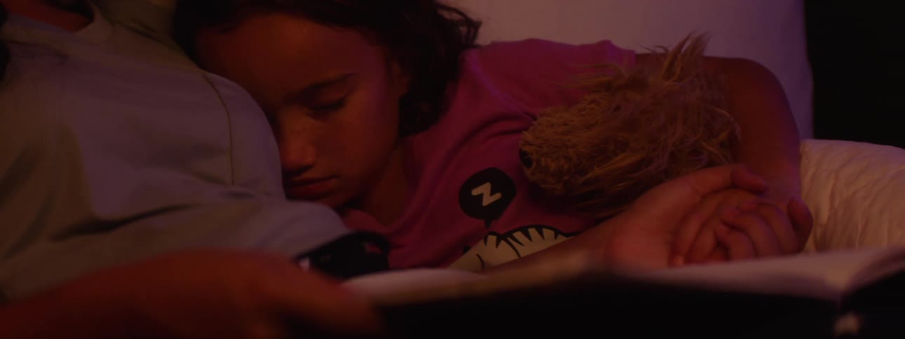 Teenage girl reads to her younger sister to sleep in a bed at night
