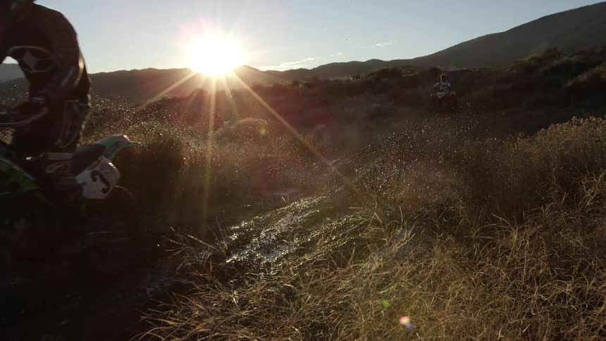 Dirt bikes riding through mud at sunset