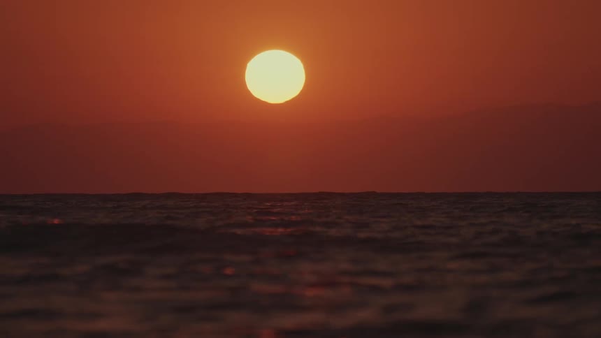 The sun glows over the water reflecting on the ripples and waves under a deep red sky
