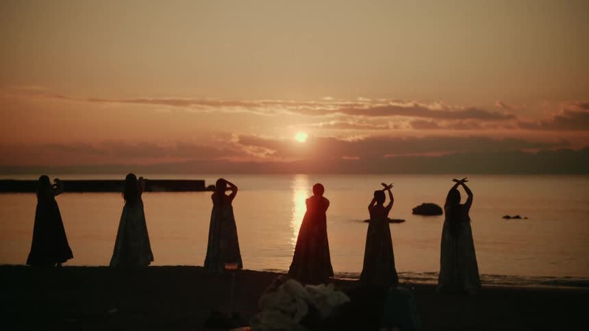 Group of women dance in a line on the beach at sunset
