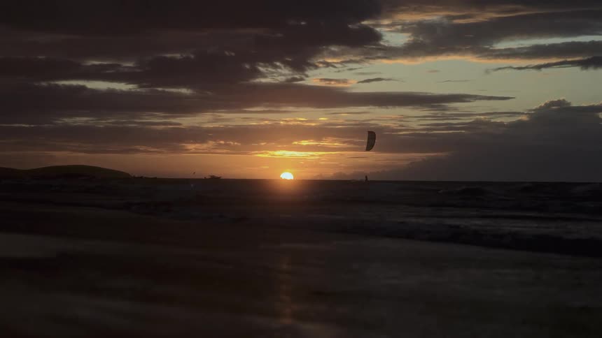 Setting sun casts a paraglider into silhouette near the coast