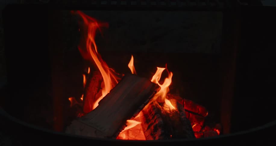 Logs crackle in a glowing fire pit flames dancing warmly in the dark