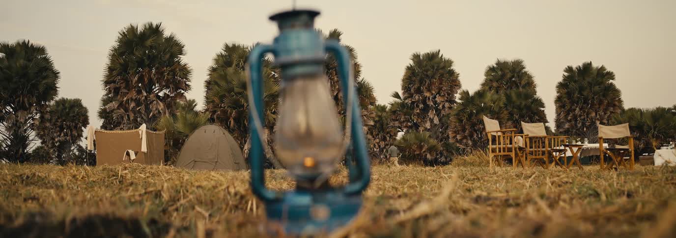 Blurred blue lantern in front of a grassy campsite with tents and chairs