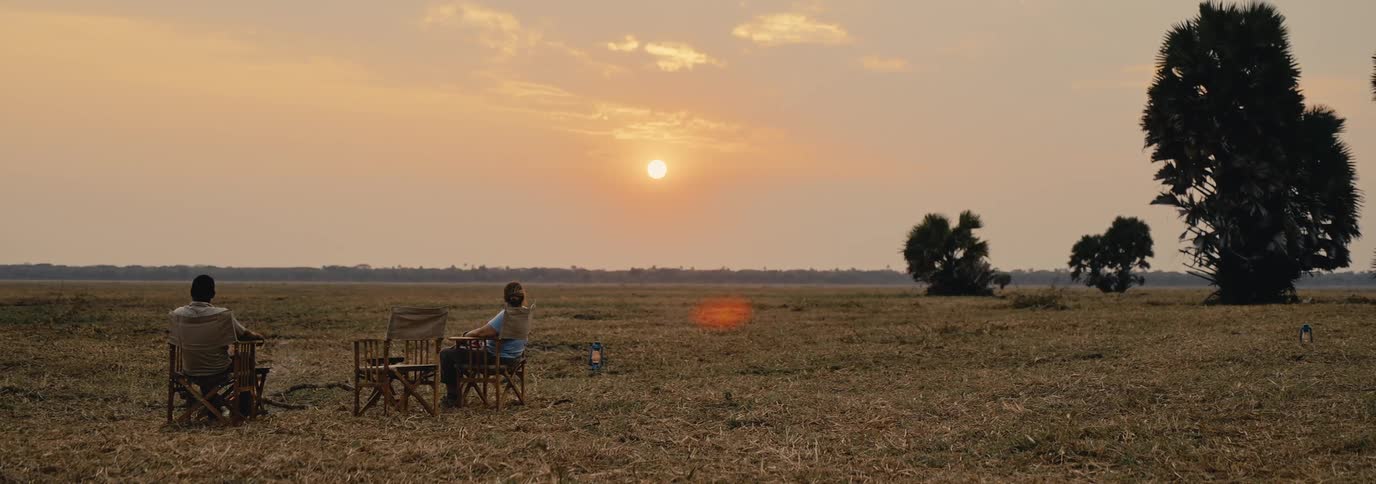 Two people relax in chairs on a dry plain watching the sunset in a peaceful open landscape