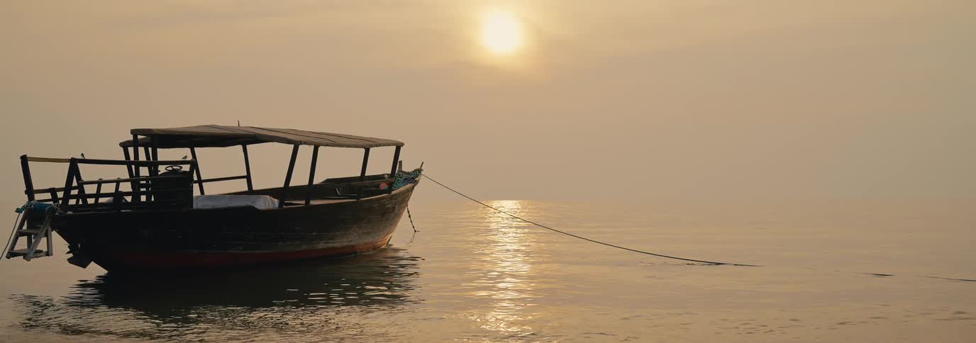 A wooden boat is calmly anchored on a still body of water at sunset