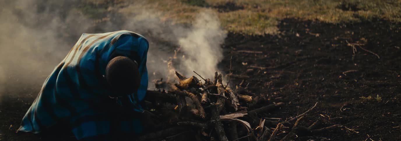 Person crouching down lighting a fire outdoors
