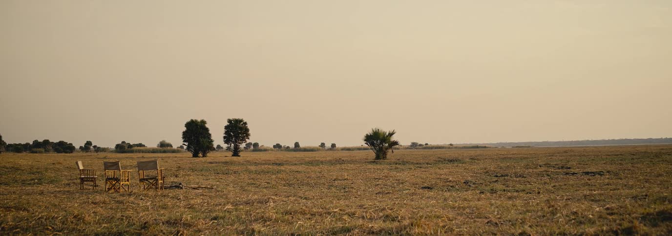Empty chairs sit in a vast dry grassland under a hazy sky