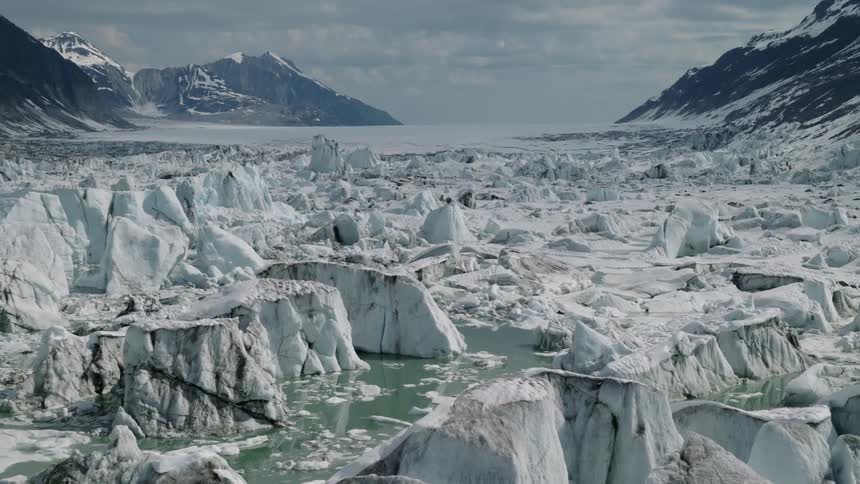 A frozen glacier field stretches between tall mountains under clouds