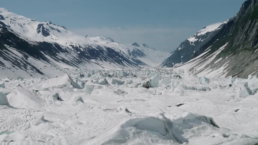 A frozen valley lies between rugged mountains under a clear sky