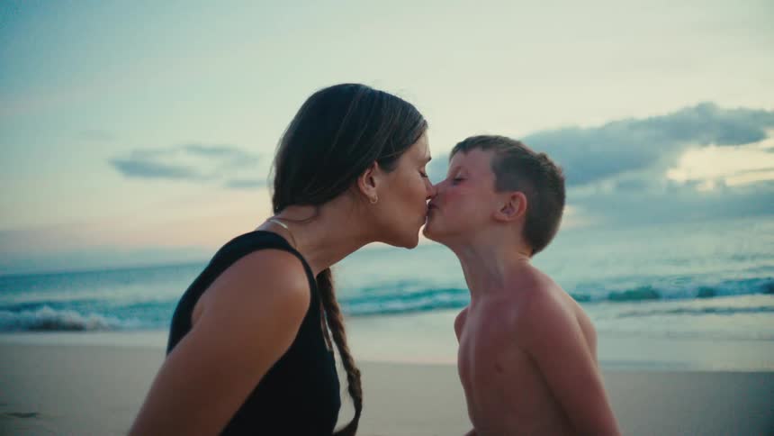 A mother and son share aaffectionate kiss on the beach at sunset