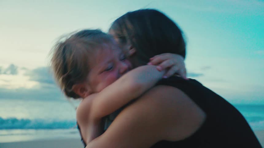Mother and daughter hug and smile warmly at the beach