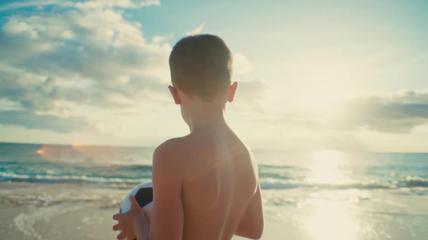 Young boy holding soccer ball near the ocean
