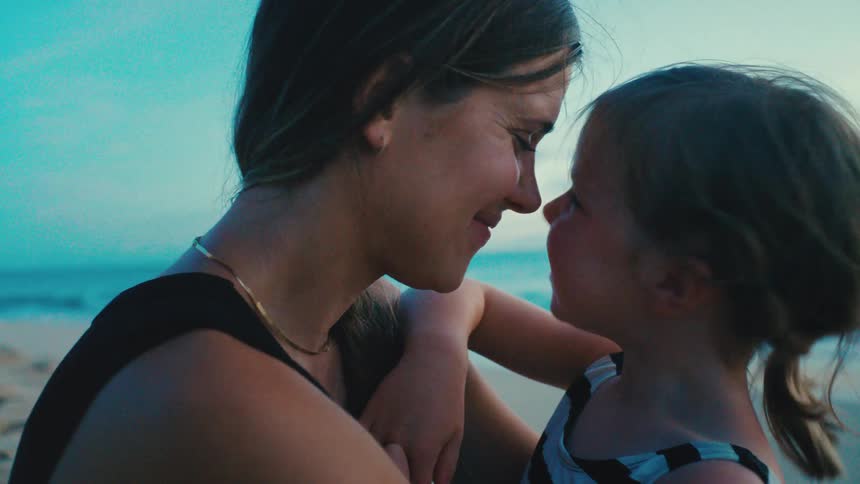 Mother and daughter share a tender moment smiling as they touch noses at the beach