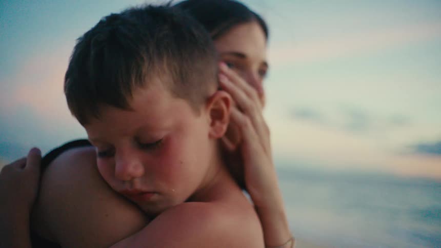 Son rests on a mother shoulder in a beach sunset embrace