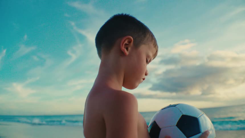 Shirtless boy holding a soccer ball while standing on a beach
