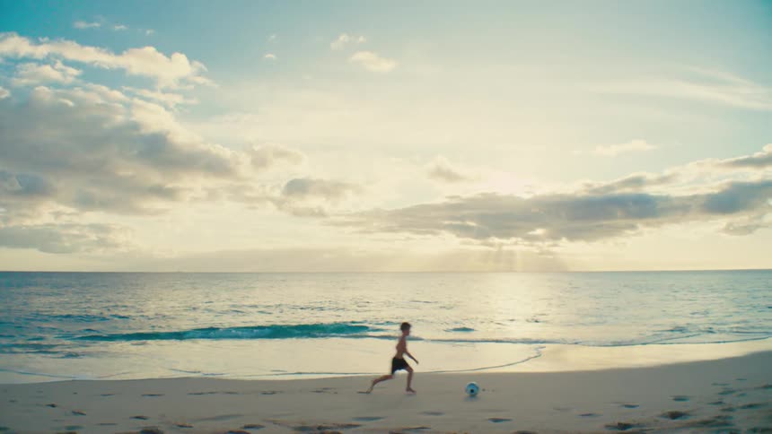 Boy playing soccer alone on the beach sand