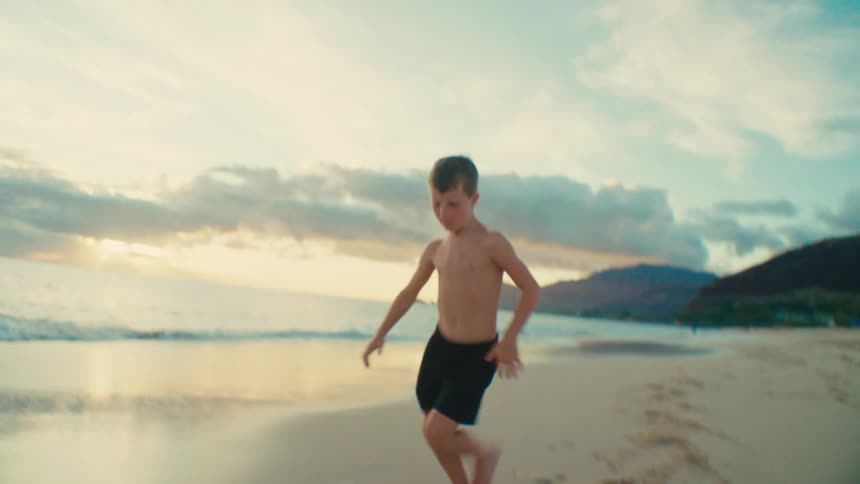 A boy kicks and runs after a soccer ball while playing at the beach during daytime