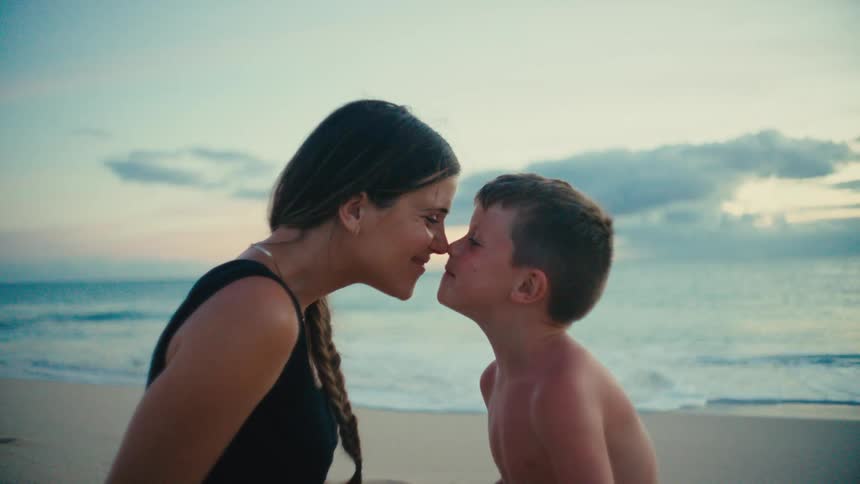 Mother and son touch noses affectionately on a beach at sunset