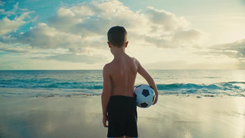 Boy facing the sea holding a ball