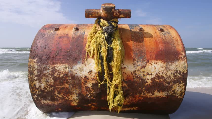 A rusty barrel in the water at the beach