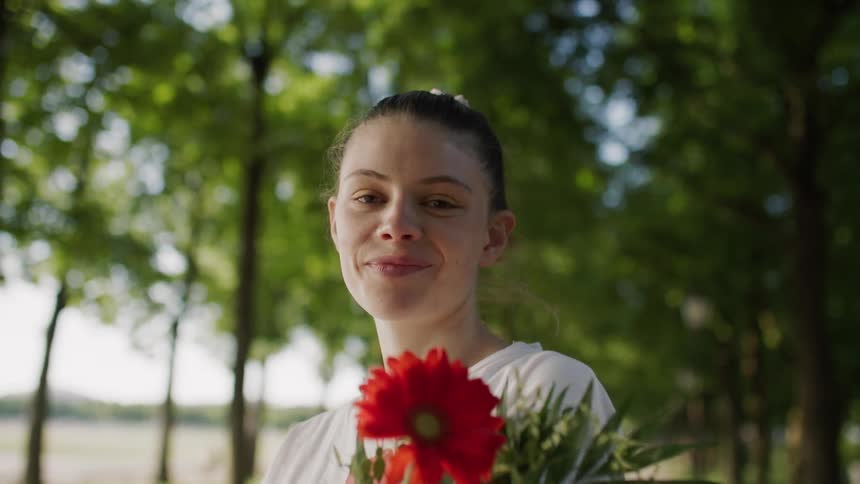 Woman in a park with trees holding a flower