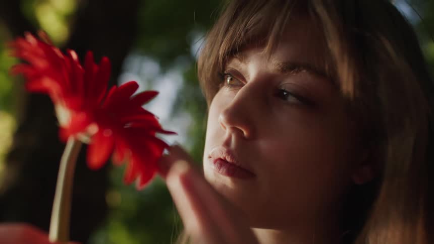 A female holding a red flower twirling and touching the flower