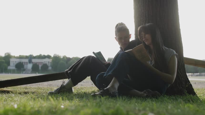 Two young people sit under a tree reading books together in a peaceful park setting