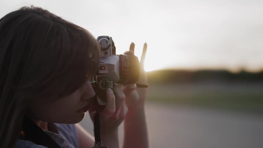 The woman is taking a photograph with her camera at sunrise