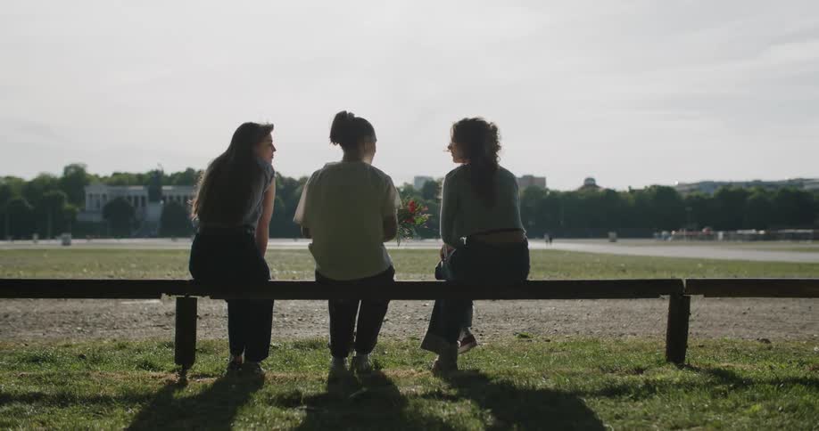 Three women chat on a park bench in a peaceful field