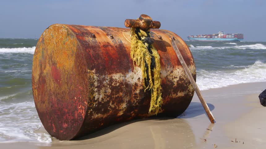 Large rusty oil drum sitting on an ocean beach