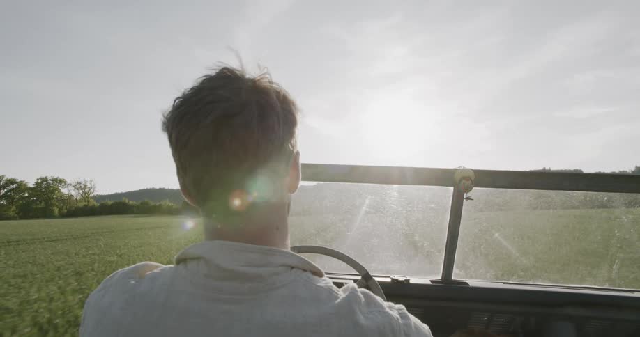 A man drives an openroof car across a grassland on a sunny day