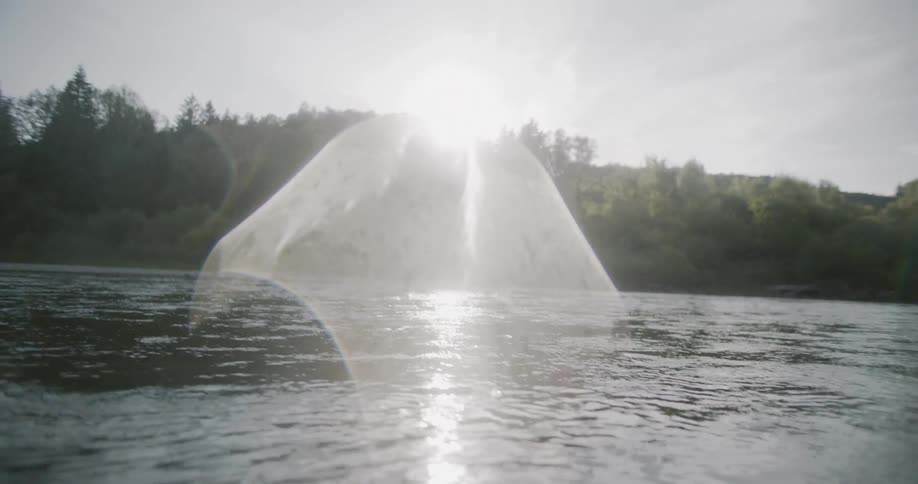 A calm river at water level reflects sunlight with a forested backdrop