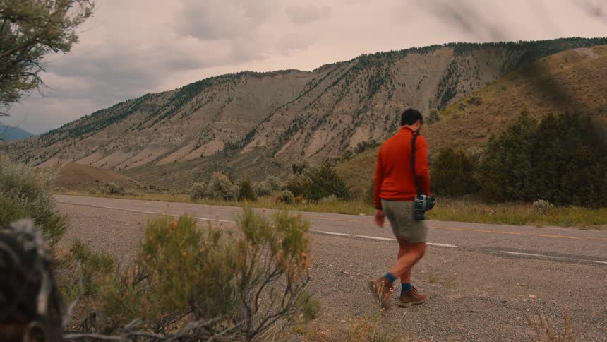 Man walking on a paved road surrounded by mountains