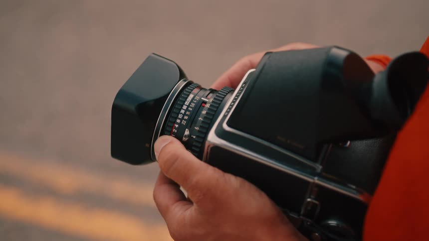 A person holds a black and silver camera with a lens hood attached adjusting the settings