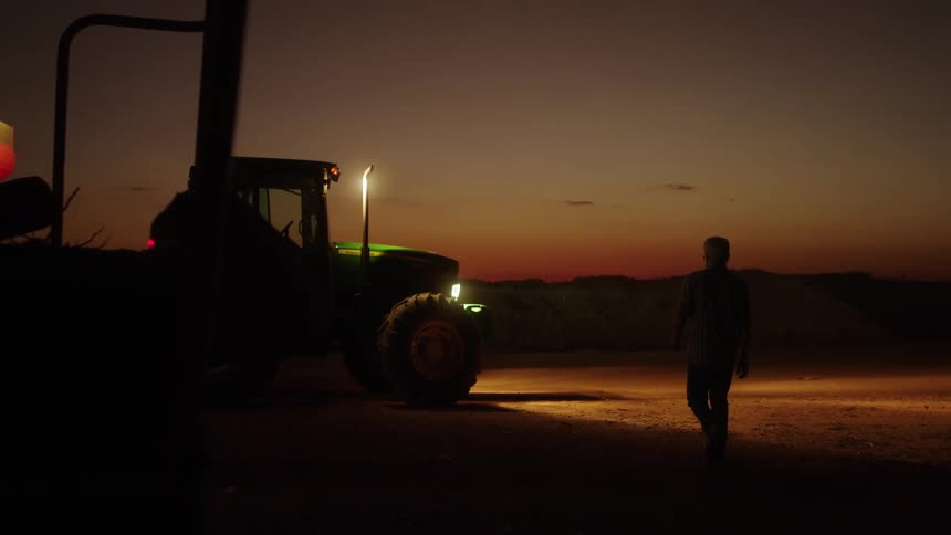 A male walking at night in front of a green tractor