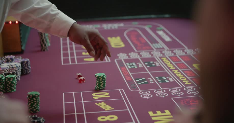 A person placing chips on a table with numbers and another person with a stick touching the table