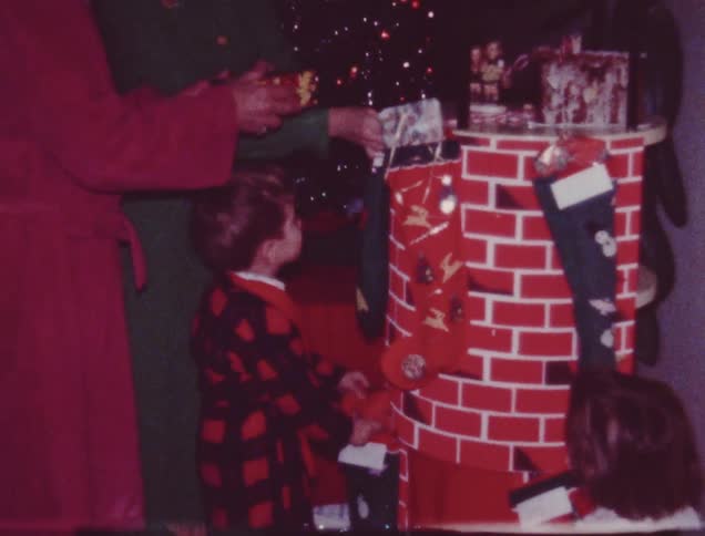 A man and woman watch kids opening presents on christmas morning