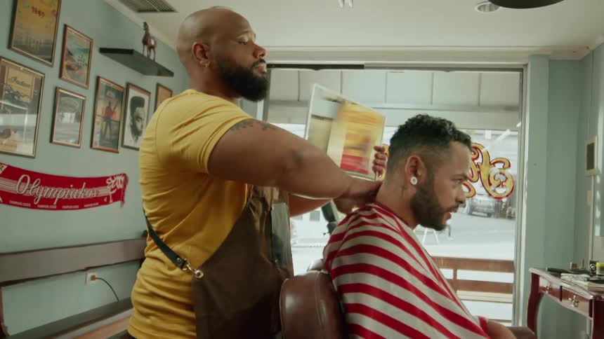 A barber holds a small mirror behind a mans head who is sitting on a chair so he can check out his haircut in the shop