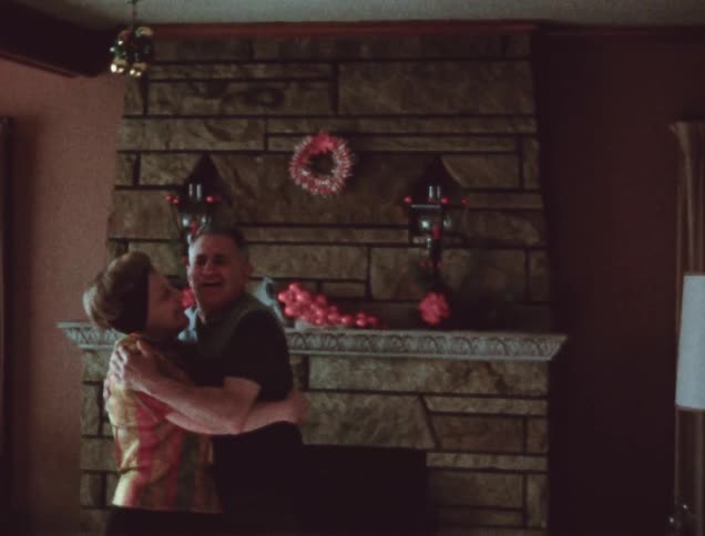 Two people kiss by a fireplace