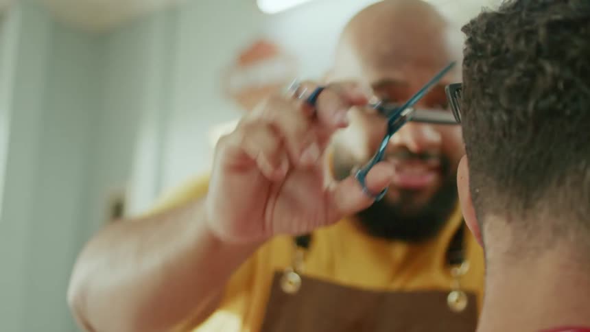 A barber is focused on cutting a customers hair with scissors in a shop