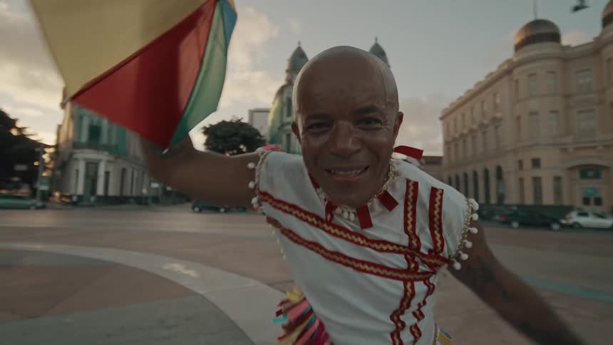 The man is dancing and waving a colorful umbrella