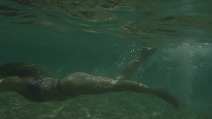 A female in water dives into the water and swims