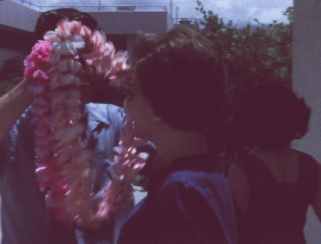 An old film of a couple kissing and putting a lei around their neck