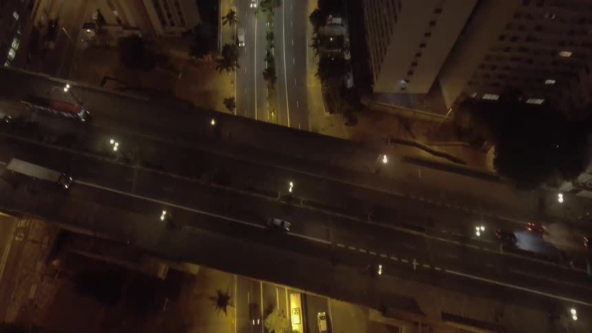 An aerial shot begins looking down on a highway at night and slowly tilts up to reveal a vast city skyline as dawn breaks