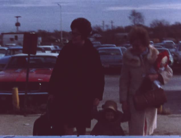 Two women walking in parking lot holding the hands of small child