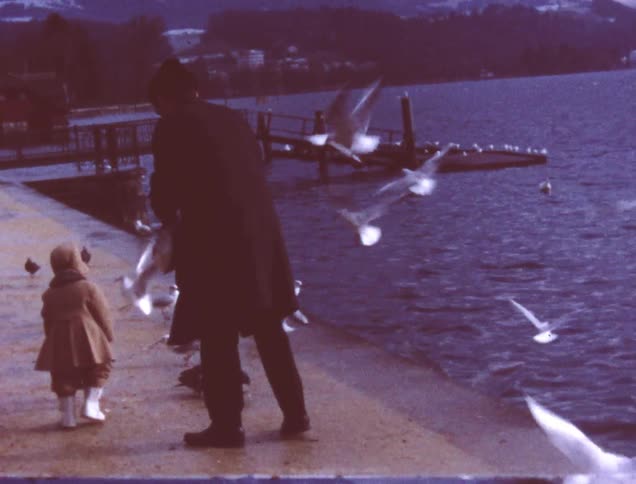 A woman and child walk feeding a flock of birds