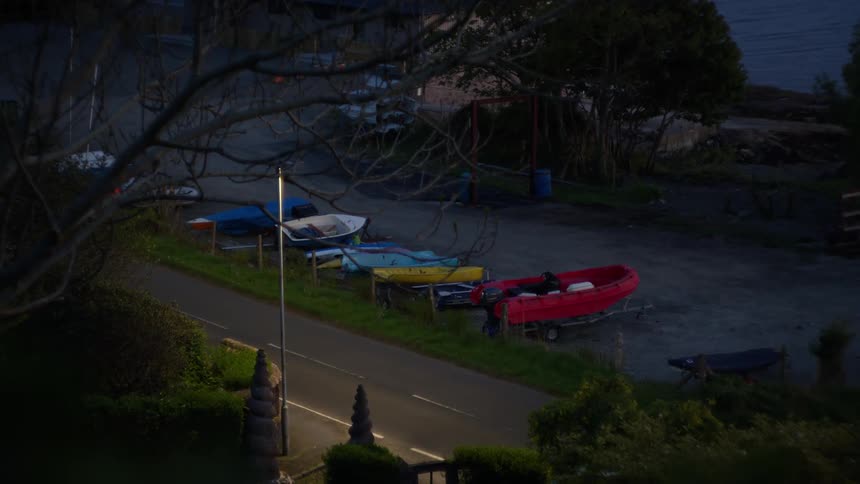 Small boats lined up beside a quiet coastal road at dusk