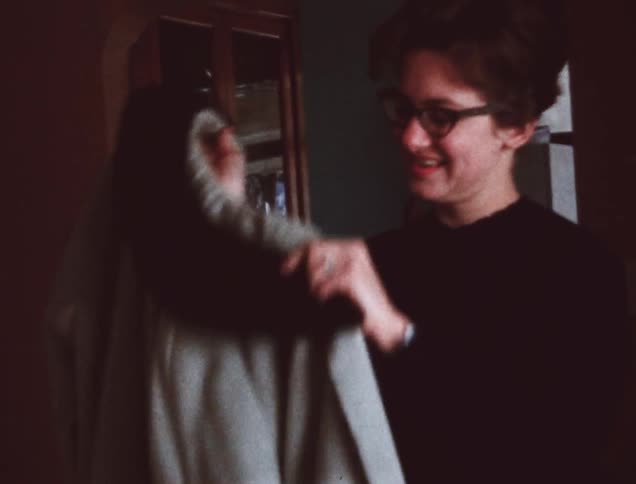 Woman holds up a coat and puts it on